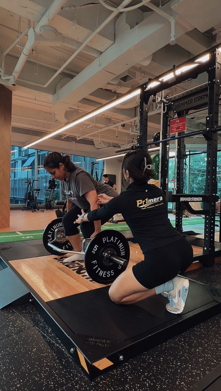 Patricia kneeling beside a client setting up a trap bar deadlift in the studio.